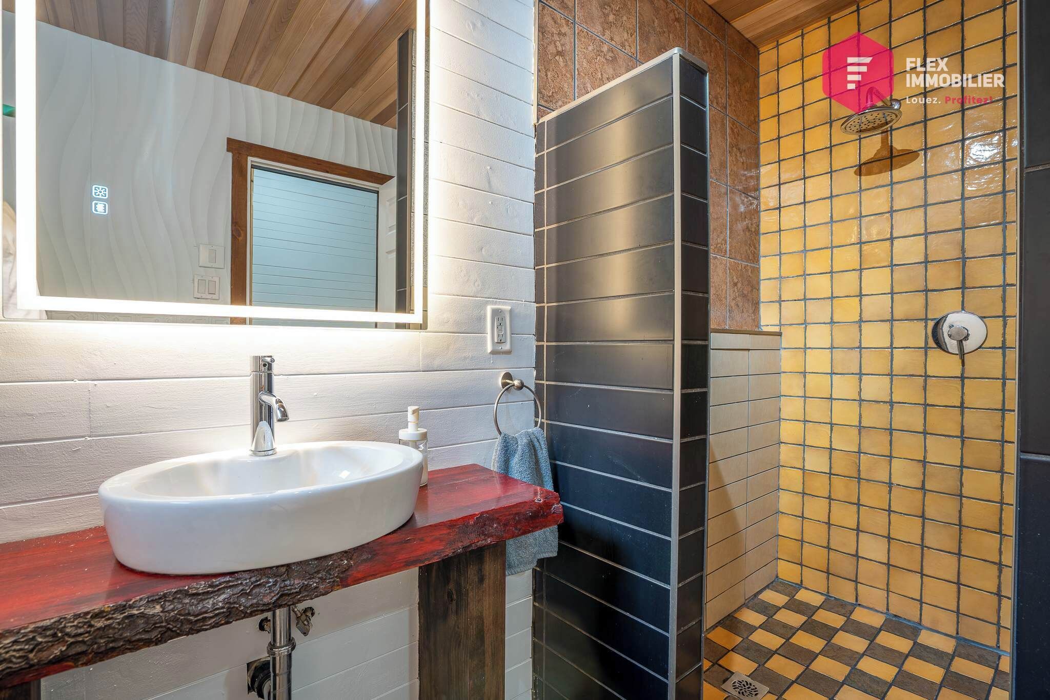 Une salle de bain avec un lavabo blanc, un miroir et un espace douche aux carreaux jaunes et noirs.