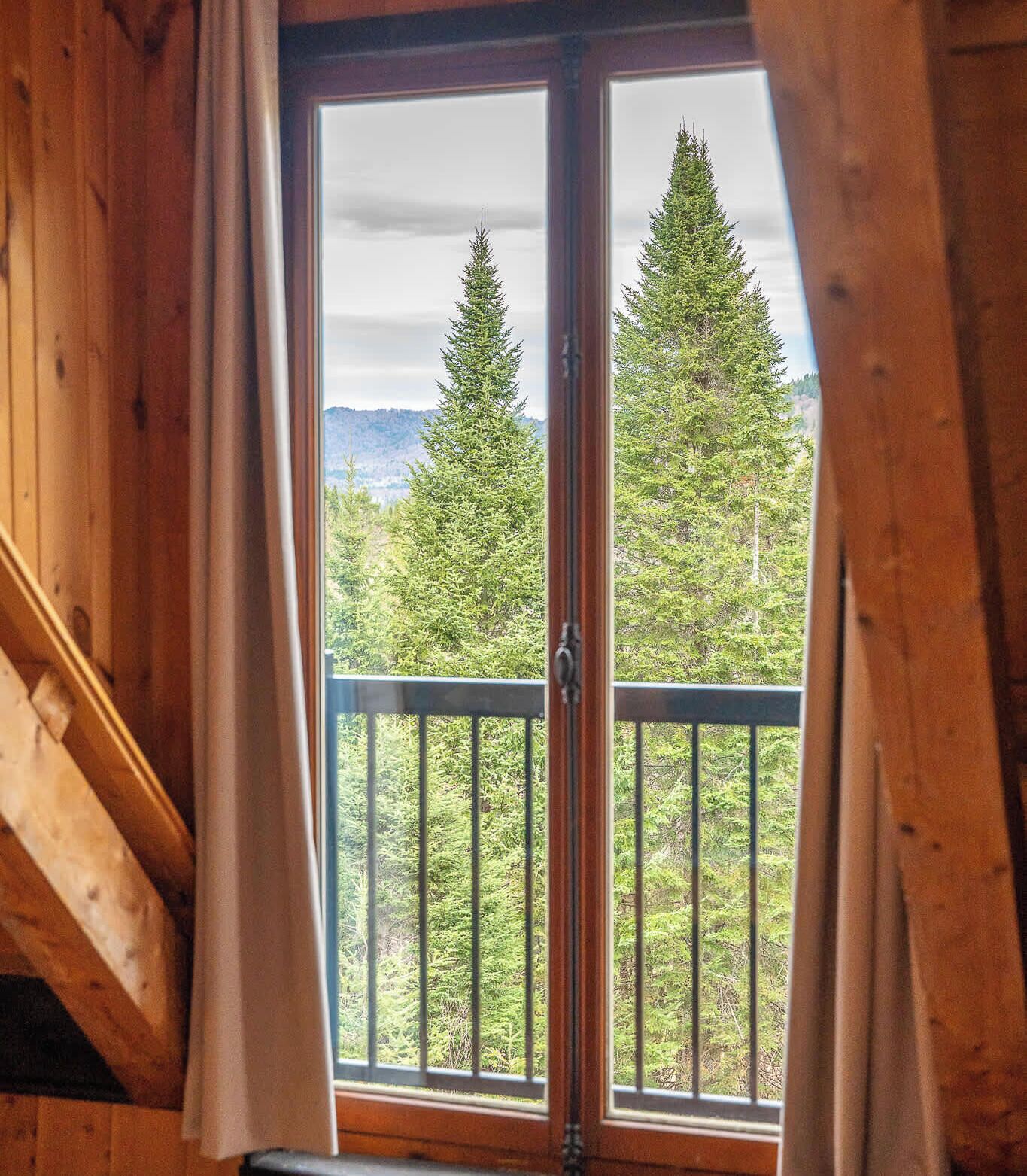 Una habitación con un amplio ventanal, paredes de madera y un balcón con barandilla.