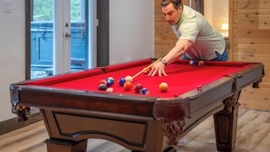 Una mesa de billar con bolas, una persona jugando y un suelo de madera.