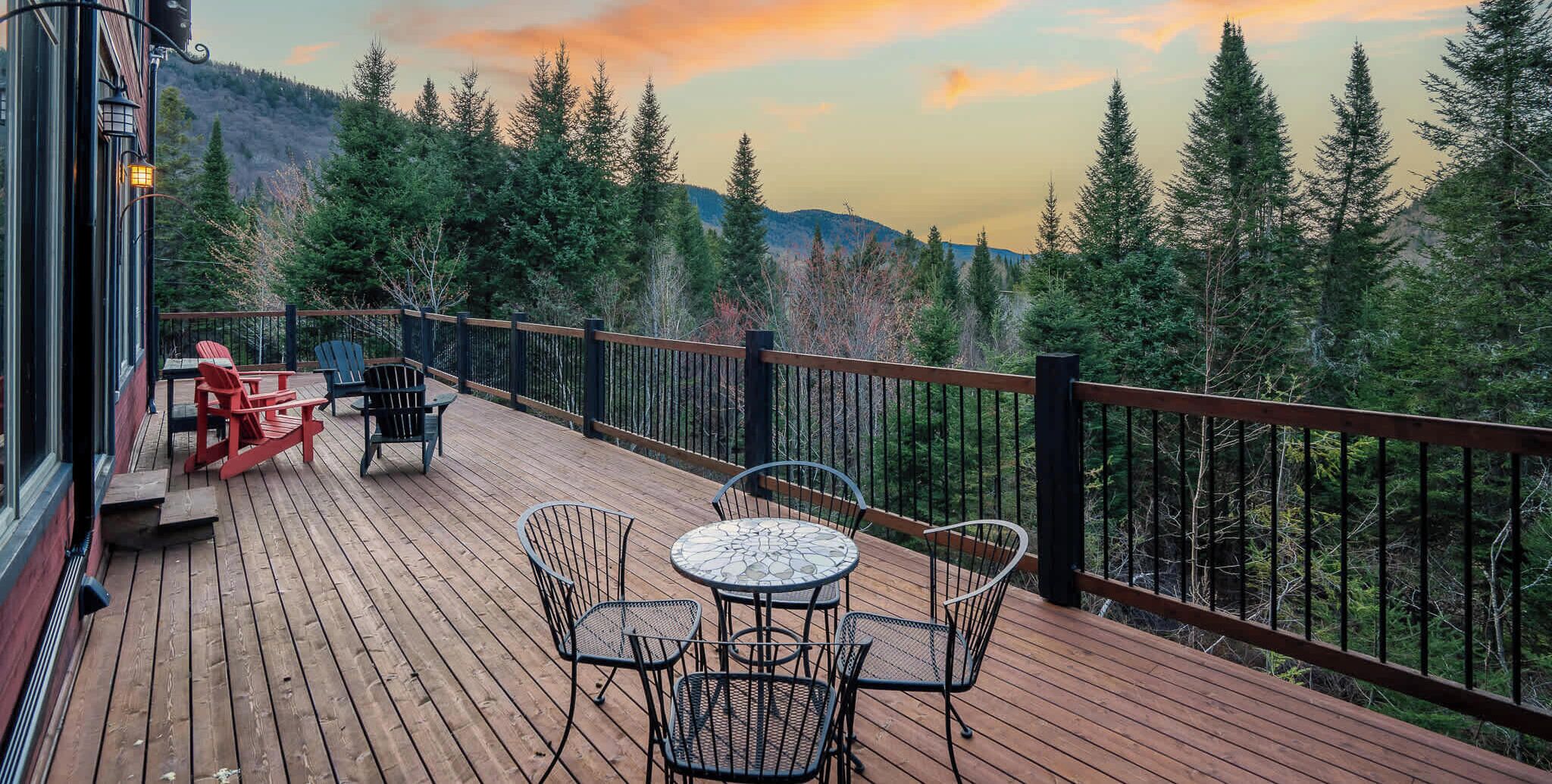 A wooden deck with outdoor seating, surrounded by a railing, overlooking a forested landscape.