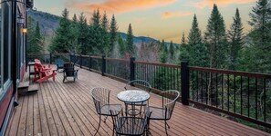 Une terrasse en bois avec des sièges extérieurs, entourée d’une rambarde, offrant une vue sur un paysage boisé.