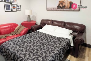 A bedroom with a brown leather sofa, a red side table, a lamp, and a bed with a patterned bedspread. - Stoneham St-Évasion, Waterfront Sauna spa for 9 (Québec)