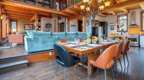 Un vaste espace de vie doté d’un plafond en bois, d’une cheminée en pierre et d’une table à manger dressée pour le repas.