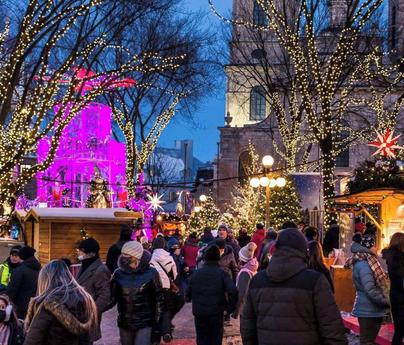 En livlig utomhusmarknad med mycket folk, försäljningsstånd och festliga dekorationer.