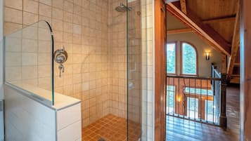 A bathroom with a glass shower enclosure, a sink, and a wooden staircase leading to an upper level.