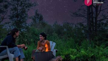 Two people sitting by a campfire in a forested area.