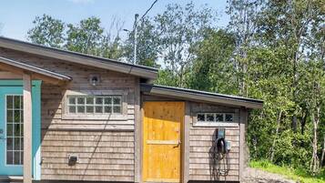 Een klein houten huisje met een turquoise deur en een gele deur, omringd door bomen.