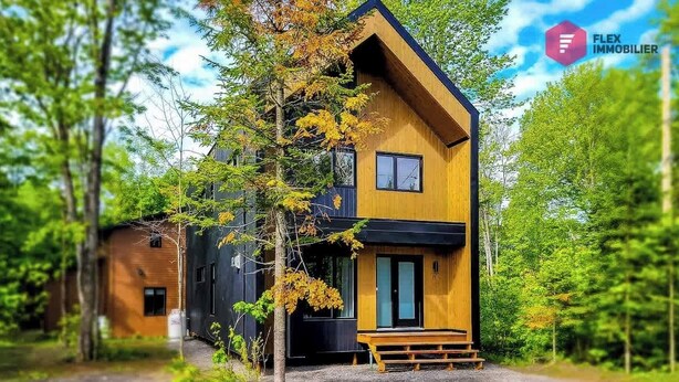 A modern wooden house with a black roof, surrounded by trees. - The Urban Flower in Portneuf - SPA, Sauna, Pool (Pont-Rouge)