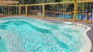 A hot tub with a wooden deck and a pool in the background. - The Urban Flower in Portneuf - SPA, Sauna, Pool (Pont-Rouge)