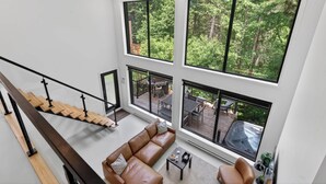 Ein modernes Interieur mit Treppe, Wohnzimmer mit Sofa und großen Fenstern mit Blick auf eine Terrasse.