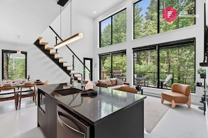 A modern interior with a kitchen island, dining area, and a staircase leading to an upper level. - The LoftWood in Portneuf - Private SPA Pool Trails (Pont-Rouge)