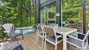Eine Terrasse mit Sitzgelegenheit im Freien, einem Whirlpool und einer Glaswand mit Blick auf den Wald.