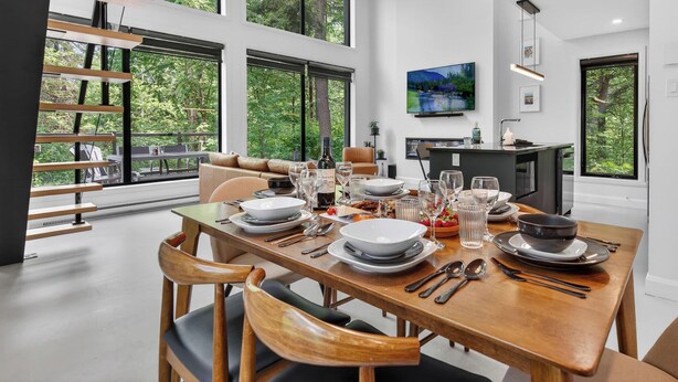 Ein Essbereich mit großem Esstisch, gedeckt für eine Mahlzeit, einer Couch und einem an der Wand befestigten Fernseher.