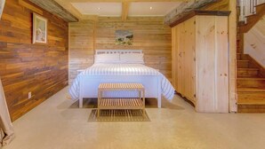 Un dormitorio con paneles de madera en la pared, una cama con ropa de cama a rayas, un banco y una escalera.