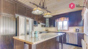 Cocina con armarios de madera oscura, una isla central con encimera de mármol, electrodomésticos de acero inoxidable y una lámpara colgante.