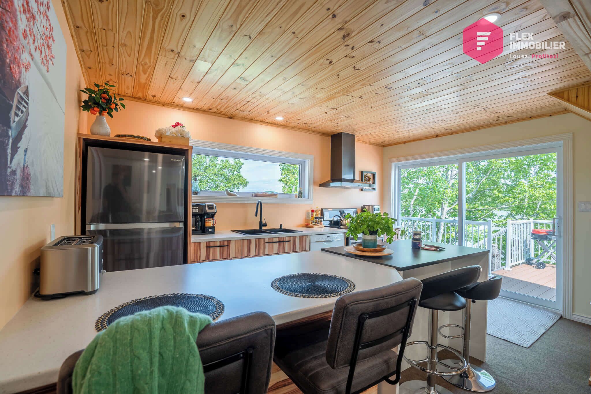 Una cocina moderna con techo de madera, refrigerador de acero inoxidable y una isla grande con taburetes de bar.