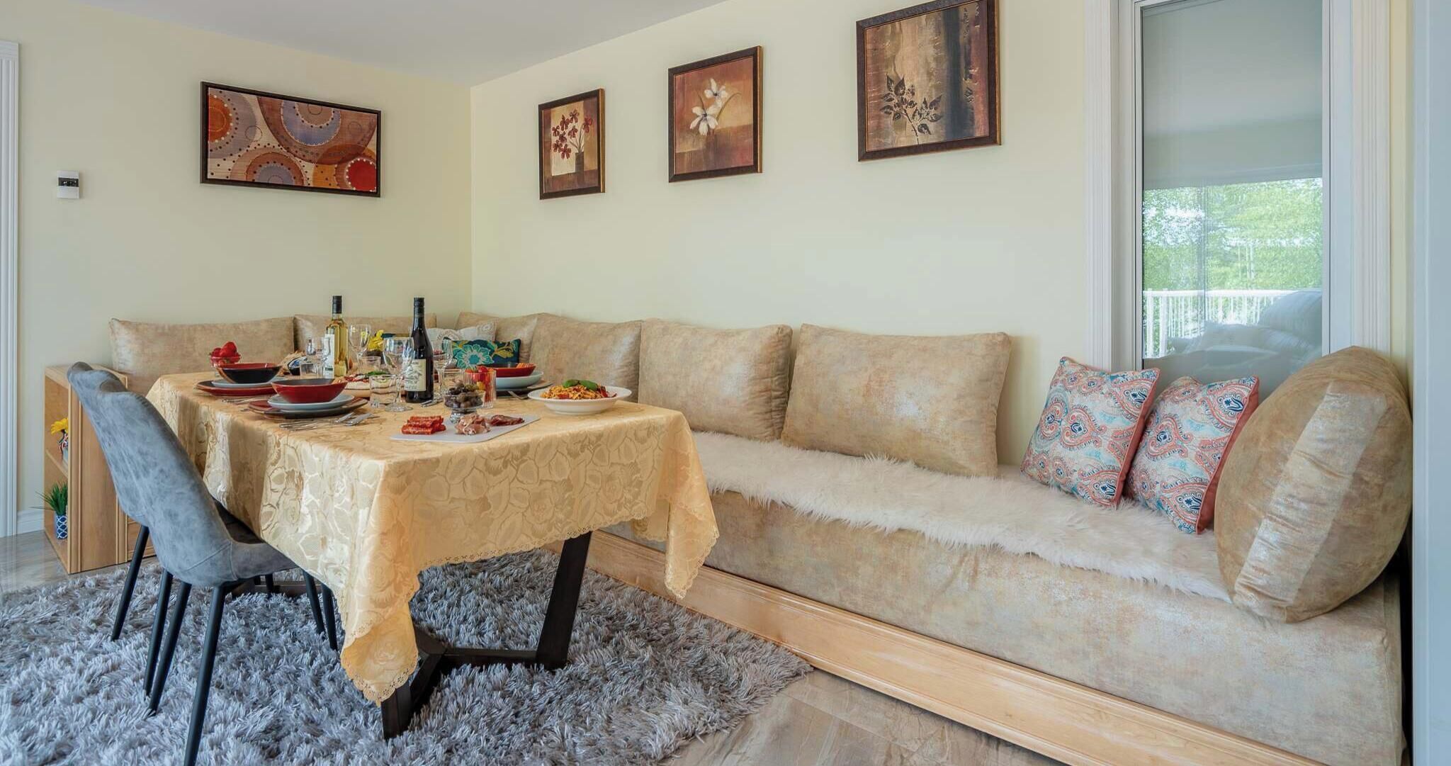 Uma sala de jantar com uma mesa posta para quatro pessoas, um sofá com almofadas estampadas e obras de arte nas paredes.