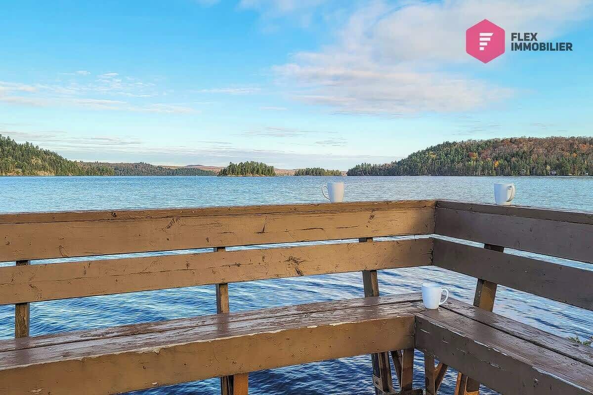 Un banc en bois donnant sur un lac paisible, avec des arbres à l’horizon et un ciel dégagé.
