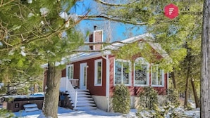 Una casa roja con un porche blanco y escalones, rodeada de nieve y árboles.