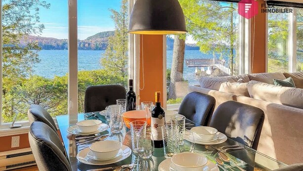 Mesa de comedor preparada para cuatro personas, con vista a un lago y colinas.