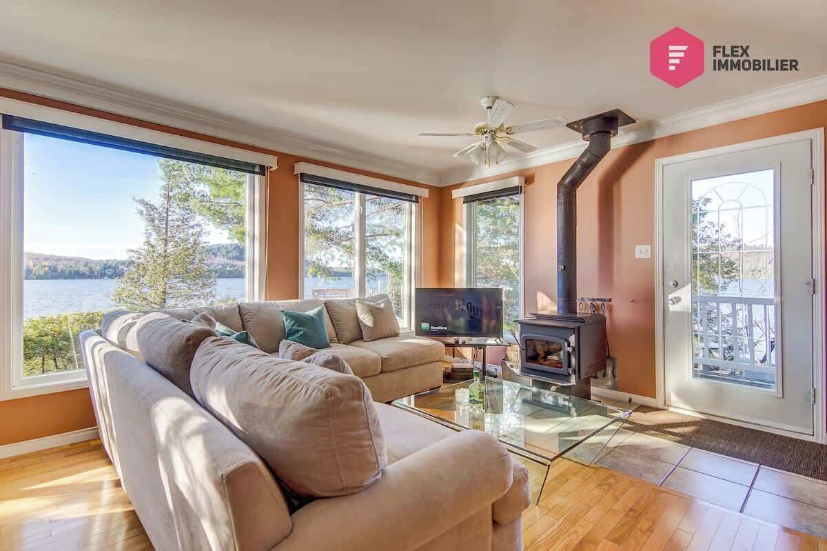 Una sala de estar con sofá, televisión, chimenea y ventanas amplias con vista a un cuerpo de agua.