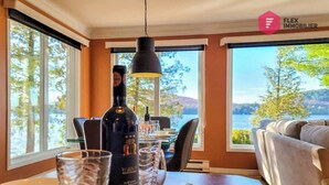 Un comedor con una mesa dispuesta para dos personas, una botella de vino y vistas a un lago a través de amplios ventanales.
