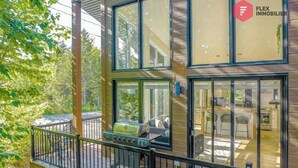 Una casa moderna con terraza, una parrilla y un amplio ventanal con vistas a un jardín.