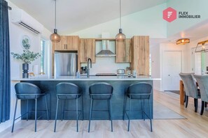 Une cuisine moderne avec des meubles en bois, un réfrigérateur en acier inoxydable et un coin bar équipé de trois tabourets.