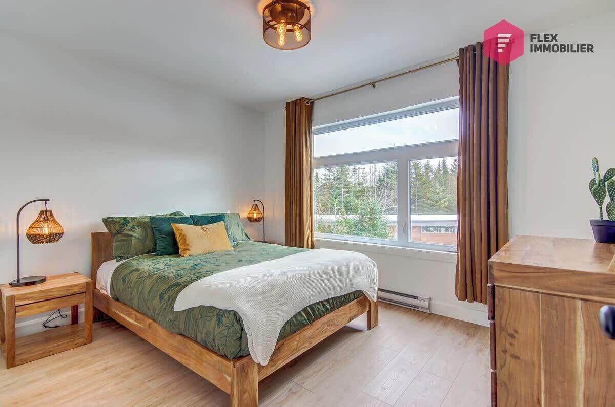 Une chambre à coucher avec un lit en bois, deux lampes de chevet, une fenêtre avec des rideaux et une vue sur les arbres.