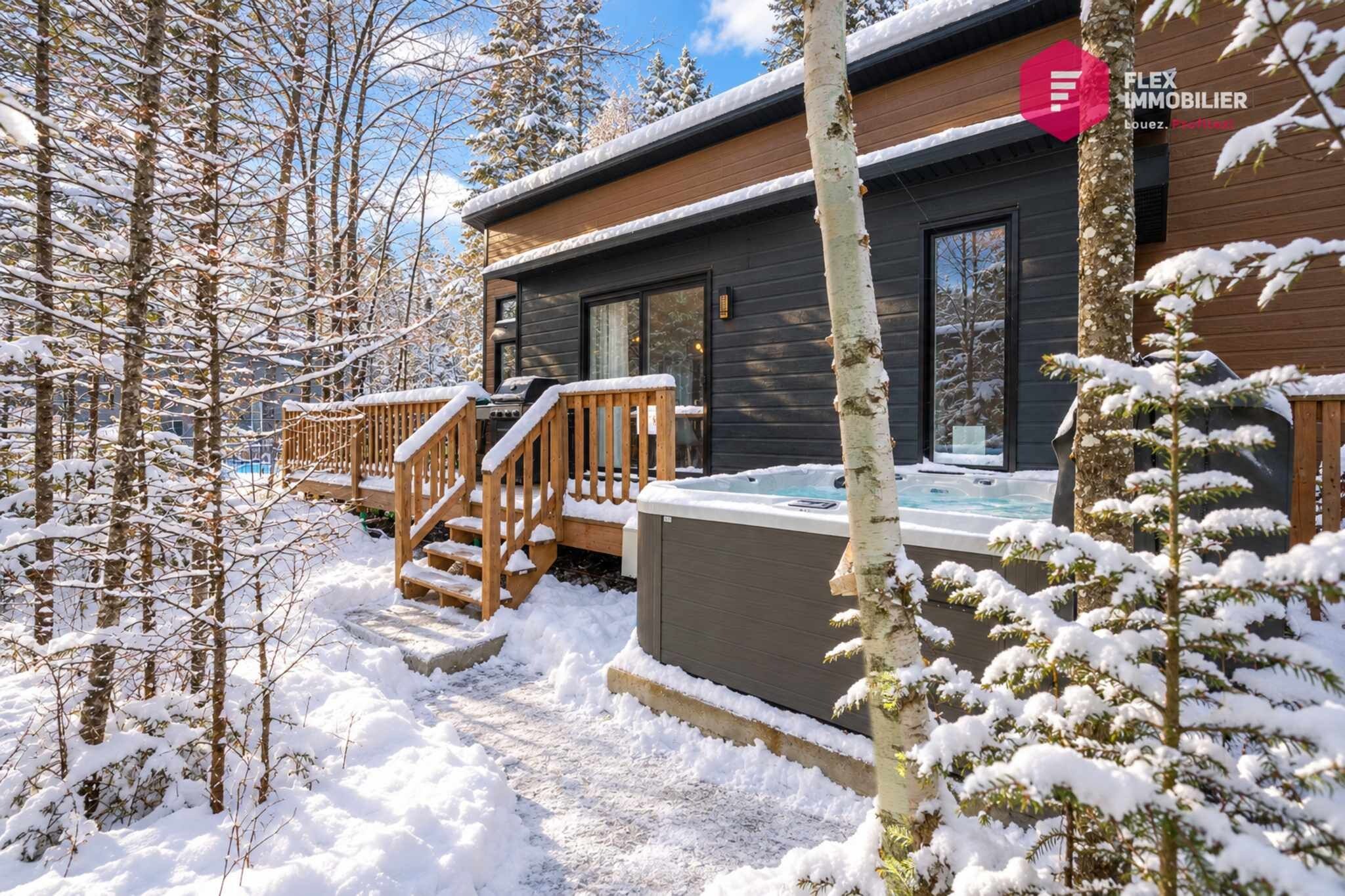A modern wooden cabin with a hot tub and a deck.