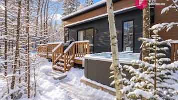 A modern wooden cabin with a hot tub and a deck.