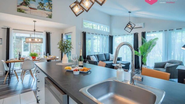 A modern kitchen with a central island, stainless steel appliances, and pendant lighting. - The Palm Tree of Portneuf - Private SPA Pool Trail (Pont-Rouge)