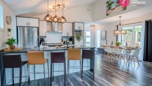 A modern kitchen with a central island, bar stools, and pendant lighting. - The Palm Tree of Portneuf - Private SPA Pool Trail (Pont-Rouge)
