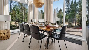A dining area with a large table, chairs, and a view of trees through large windows.