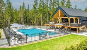 Un espace piscine doté d’une terrasse en bois, de chaises longues et de parasols.
