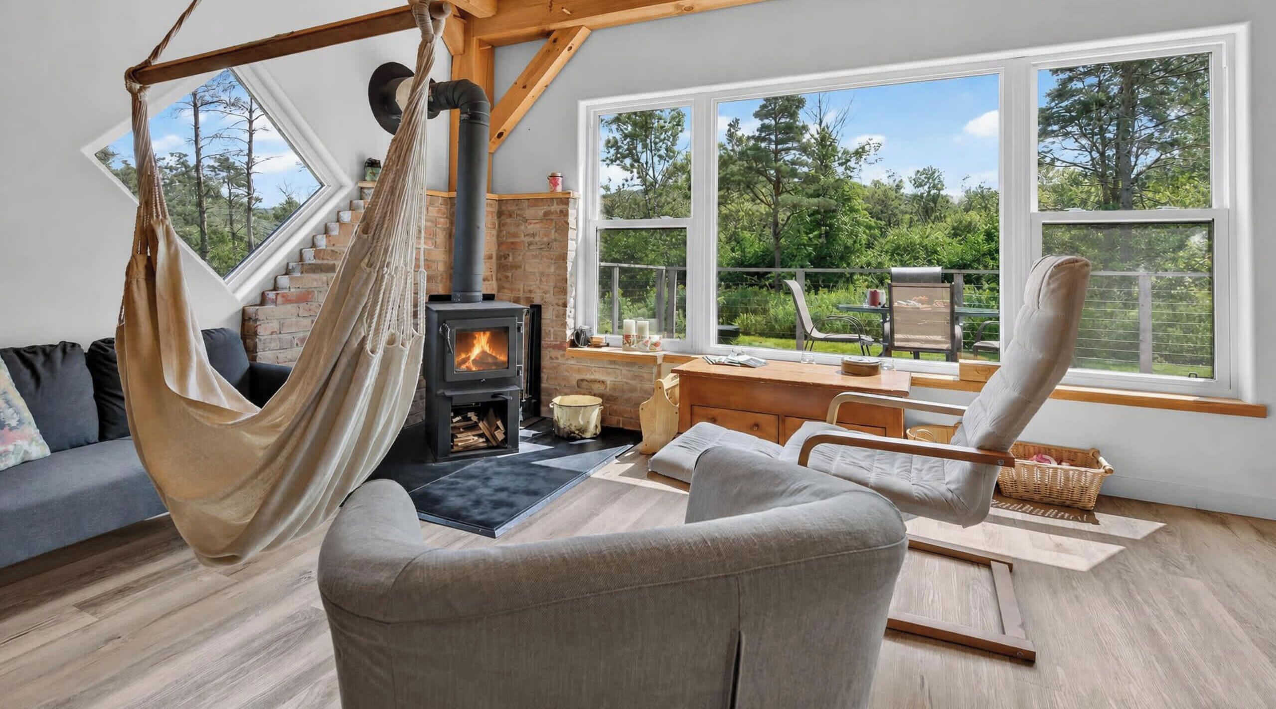A cozy living room with a hammock, a fireplace, a sofa, and a dining area with a view of the outdoors.