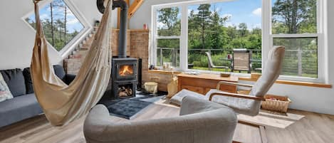 Ein gemütliches Wohnzimmer mit einer Hängematte, Kamin, einer Couch und einem Essbereich mit Blick ins Freie.