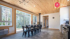 A spacious room with large windows, a dining area with chairs, a kitchen with a stove, and a ceiling with wooden beams. - The Singing Salmon of Bonaventure - A wild escape (Bonaventure)