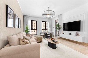 A modern living room with a beige sofa, a coffee table, and a flat-screen TV mounted on the wall. - Stayshort - 1 Bed in Old Town Downtown That Sleeps 4 and Close to Burj Khalifa (Dubai)