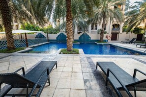 A pool area with lounge chairs and palm trees. - Stayshort - 1 Bed in Old Town Downtown That Sleeps 4 and Close to Burj Khalifa (Dubai)