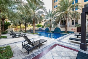 A poolside area with lounge chairs, palm trees, and a swimming pool. - Stayshort - 1 Bed in Old Town Downtown That Sleeps 4 and Close to Burj Khalifa (Dubai)