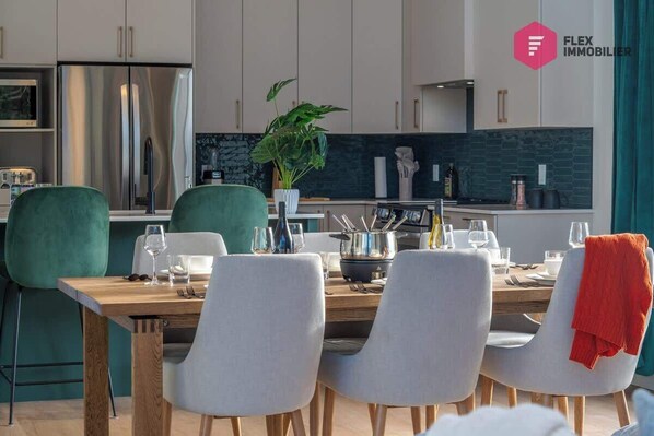 A modern kitchen with stainless steel appliances, a dining area with a wooden table and chairs, and a potted plant on the counter.