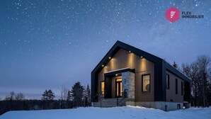 Une maison moderne avec une façade en pierre, de grandes fenêtres et un revêtement extérieur en bois.