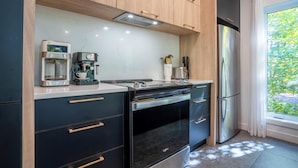 Una cocina moderna con cafetera espresso integrada, refrigerador de acero inoxidable y ventana con vistas a zonas verdes.