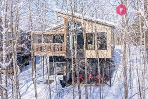 Eine zweistöckige Holzhütte mit Balkon, umgeben von schneebedeckten Bäumen.
