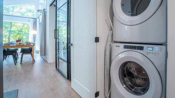 A laundry room with a front-loading washing machine and dryer, a dining area with a table and chairs, and a view through a glass door. - King bed, Cinema screen, Private SPA, Near Quebec (Pont-Rouge)