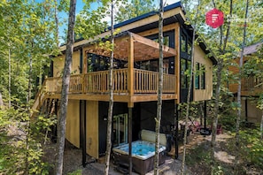 A two-story wooden cabin with a balcony, a hot tub, and a deck surrounded by trees. - King bed, Cinema screen, Private SPA, Near Quebec (Pont-Rouge)
