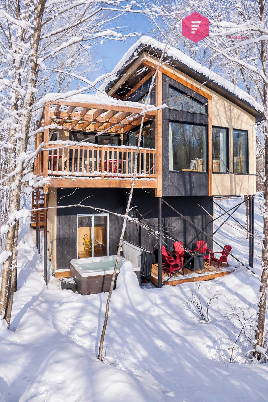 Une cabane à deux étages avec un balcon, un jacuzzi et des chaises rouges à l’extérieur.