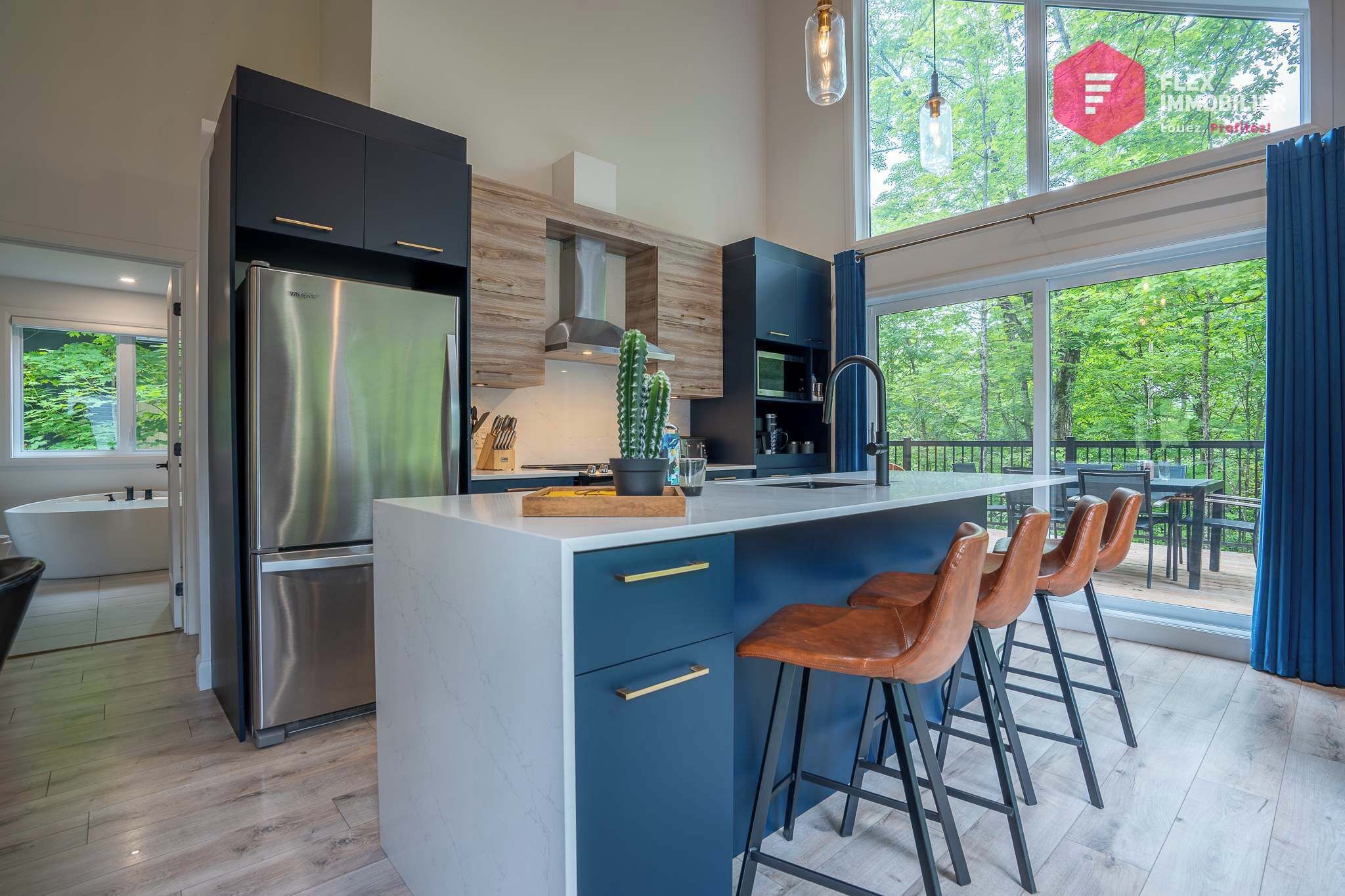 A modern kitchen with a central island, bar stools, and a view of the outdoors.