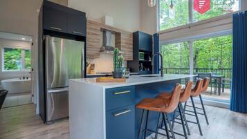 A modern kitchen with a central island, bar stools, and a view of the outdoors.